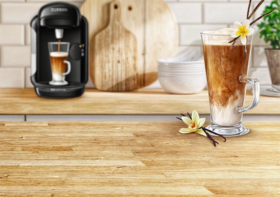 A refreshing iced coffee with a hint of vanilla sits elegantly on a wooden table, complemented by the sleek design of a TASSIMO coffee machine.