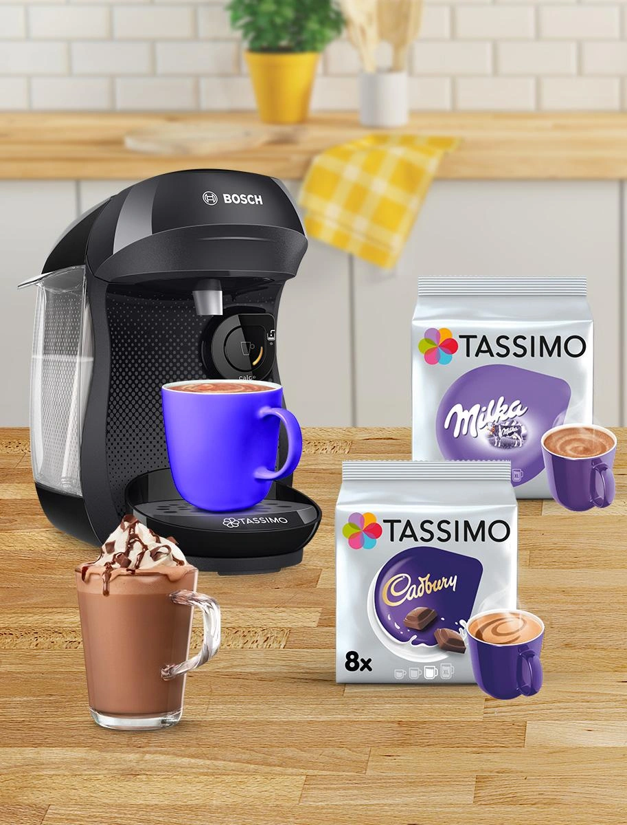 A TASSIMO coffee maker sits on the counter, accompanied by a blue mug and an assortment of Tassimo Milka and Cadbury pods.