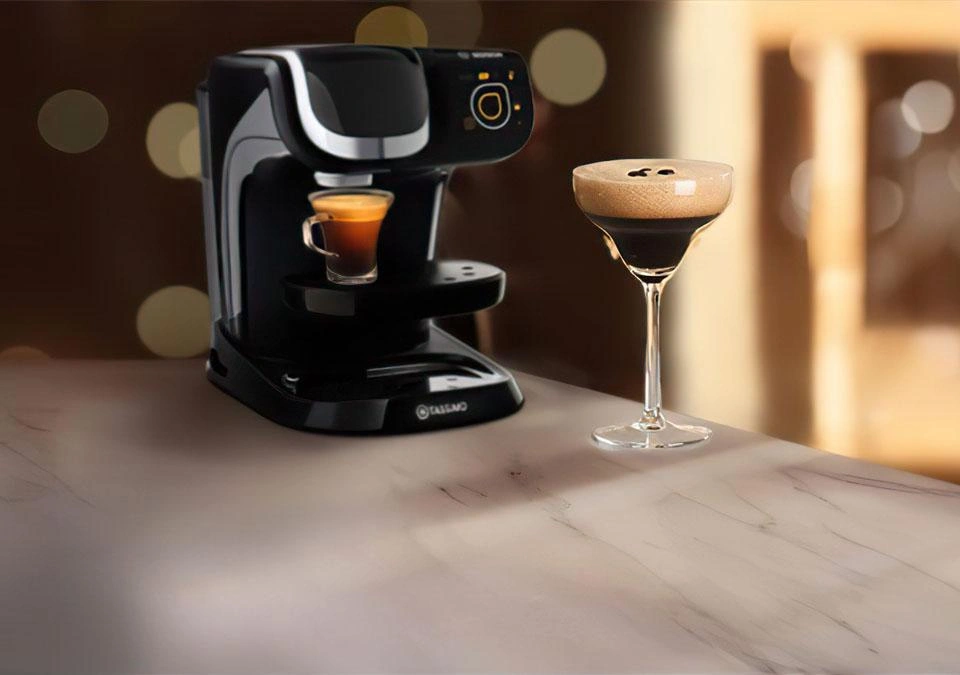 A TASSIMO espresso machine sits elegantly on the counter, accompanied by a sleek glass of espresso martini beside it.