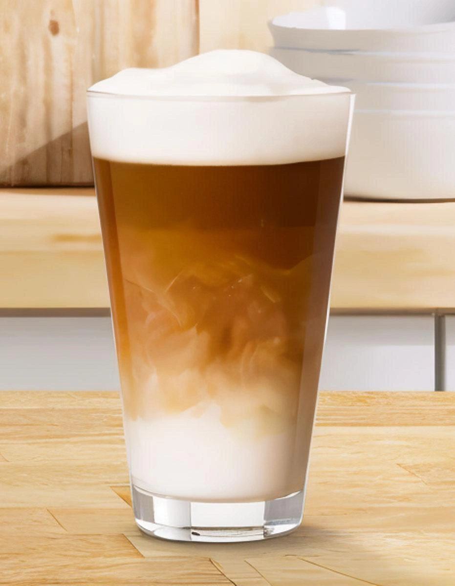 TASSIMO glass of iced coffee with milk froth on a wooden countertop.