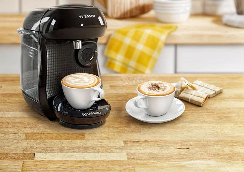 A TASSIMO coffee machine sits on a wooden countertop, poised with two cups ready for brewing.