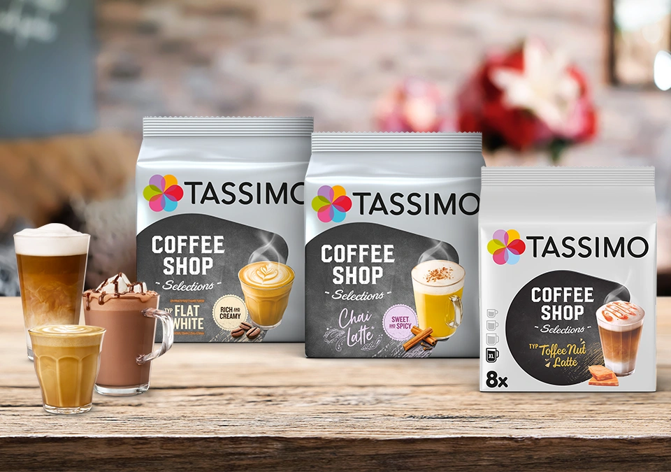 A neatly arranged display of TASSIMO coffee packets and assorted coffee drinks rests on a rustic wooden surface, showcasing a variety of flavors and aromas.