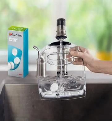 Hand filling a TASSIMO coffee maker reservoir with water and adding a Tassimo tablet.