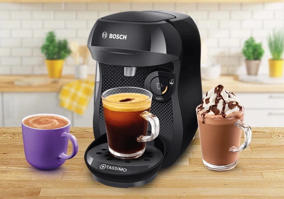 The kitchen counter features a sleek TASSIMO coffee machine, surrounded by an assortment of cups filled with various aromatic coffee drinks.