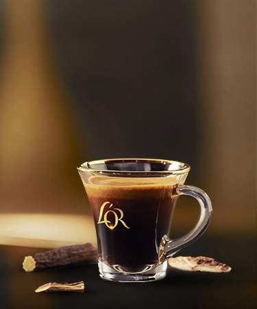 Two mugs filled with L'OR Espresso on a slate tray, with scattered coffee beans and a silver spoon for an elegant presentation.