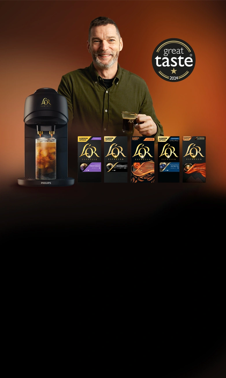 Fred Sirieix standing behind L’OR Barista Absolu machine with various L'Or capsule flavors, featuriung 'Great Taste 2024' award logo