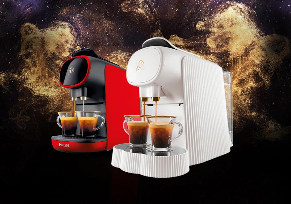 Machine à café L'OR Passione Rossa et machine à café blanche Alessi avec des tasses. Fond doré scintillant.