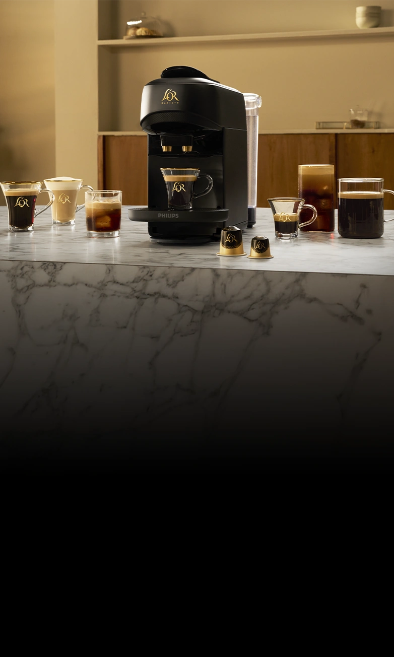 Máquina de café L'OR BARISTA y varias tazas de café sobre una encimera de mármol.