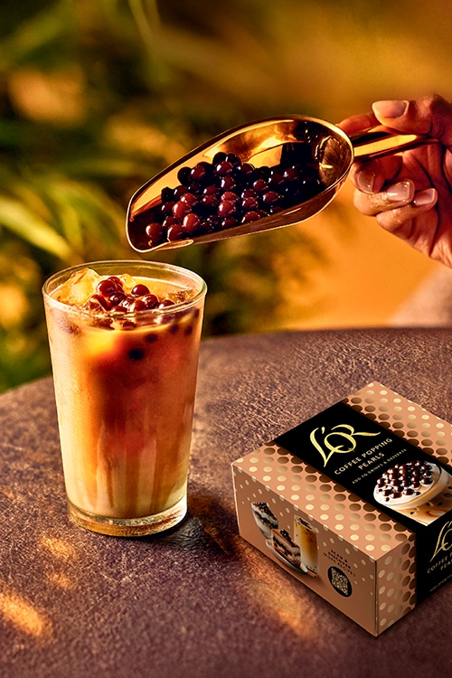 L'OR Coffee Pearls poured into an iced coffee and L'OR Coffee Pearls pack on a table.