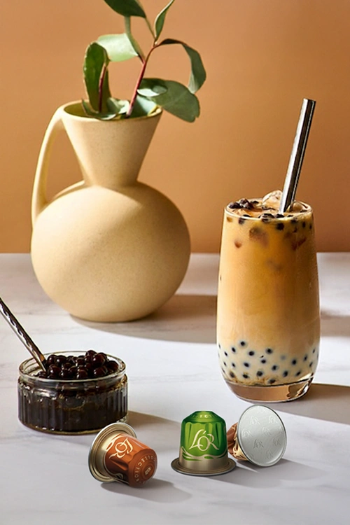 Iced coffee with L'OR Coffee Pearls inside and 3 capsules from Flavours collection on a marble table.