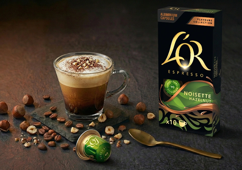 A cup of coffee next to a L'OR Espresso Hazelnut coffee capsule pack