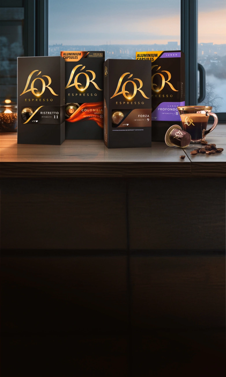 L'OR Ristretto, Colombia, Forza and Profondo packs, coffee cup and capsules on a wooden table with winter window background.