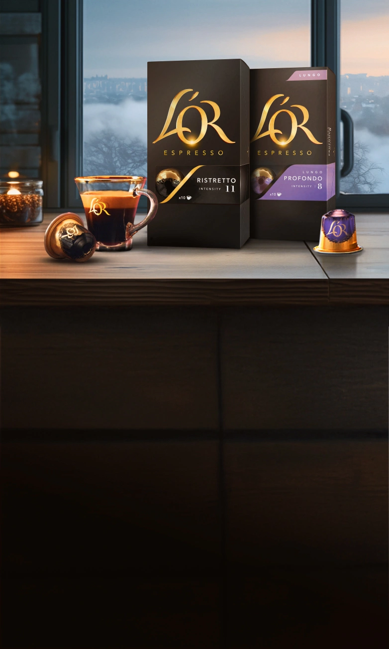 L'OR Ristretto and Profondo packs with coffee cup, capsules on a wooden table with winter window background. 