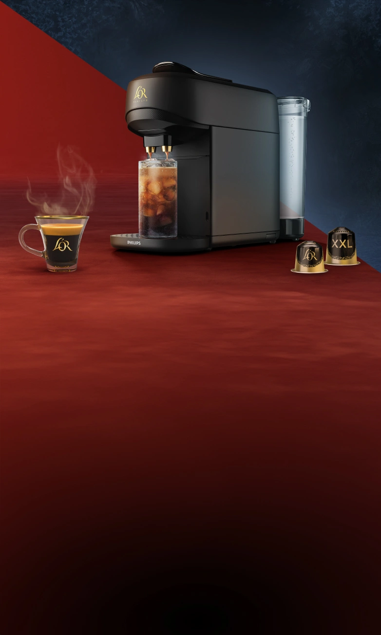 Black L'OR Absolu coffee machine, coffee cup and Ristretto capsules on a wooden table with winter window background.