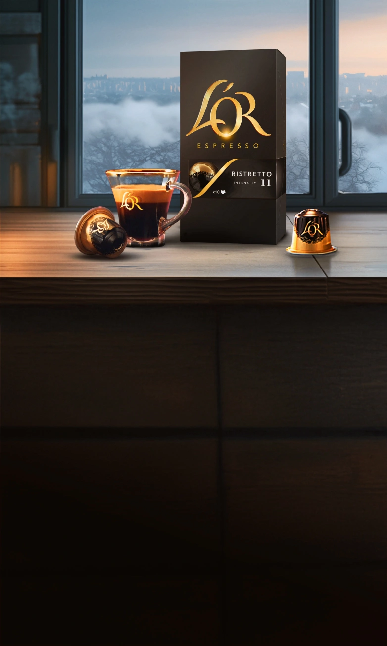 L'OR Ristretto pack with coffee cup and capsules and scattered beans on a wooden table with winter window background. 