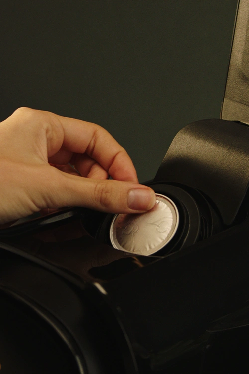 Hand inserting a coffee capsule into the top of a L’OR Barista machine.