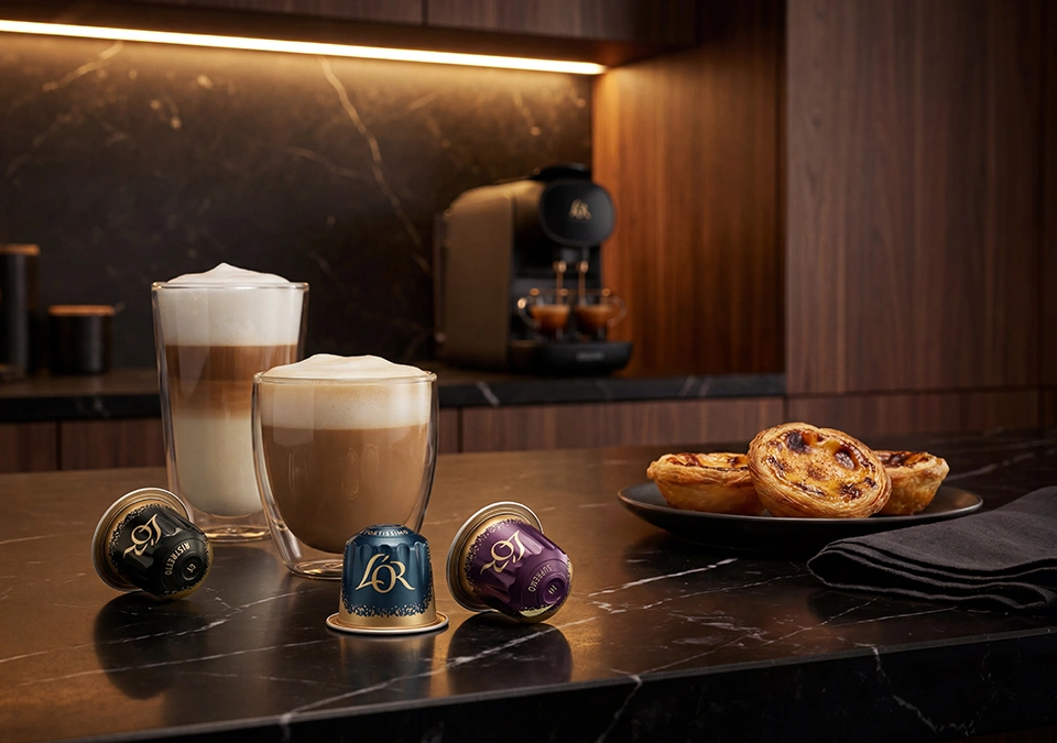 Varias bebidas de café junto a cápsulas L'OR sobre una mesa vistas desde arriba, con galletas al lado