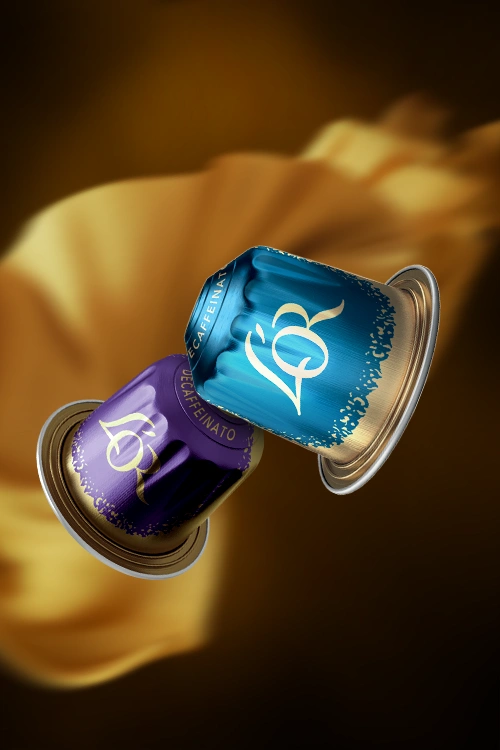 Dos cápsulas L'OR de la colección Descafeinado flotando. Tela de seda dorada al fondo.