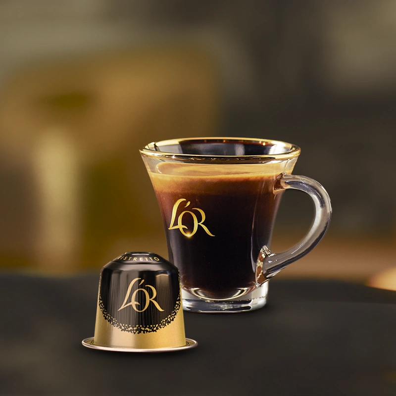 Een klein glazen ristretto-kopje en een klassieke capsule op een donkere tafel.
