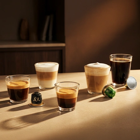 Tres tazas de café L'OR en diferentes estilos sobre una mesa, incluyendo espresso, café con leche y café negro