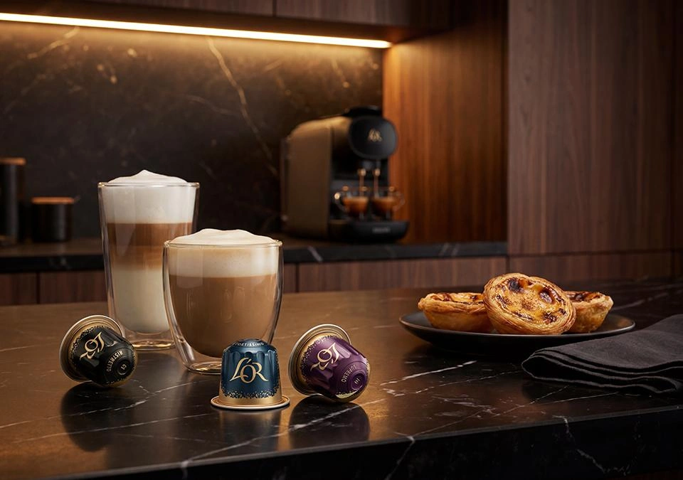 Varias bebidas de café junto a cápsulas L'OR sobre una mesa vistas desde arriba, con galletas al lado