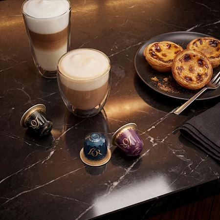 Varias bebidas de café junto a cápsulas L'OR sobre una mesa vistas desde arriba, con galletas al lado