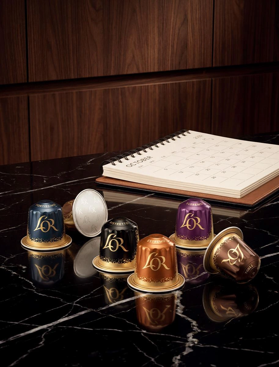 Cápsulas de café L'OR colocadas junto a una taza de espresso y un cuaderno sobre una superficie de madera