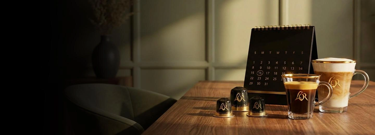 L'OR coffee capsules, an espresso and a latte macchiato next to a black desk calendar on a wooden table.