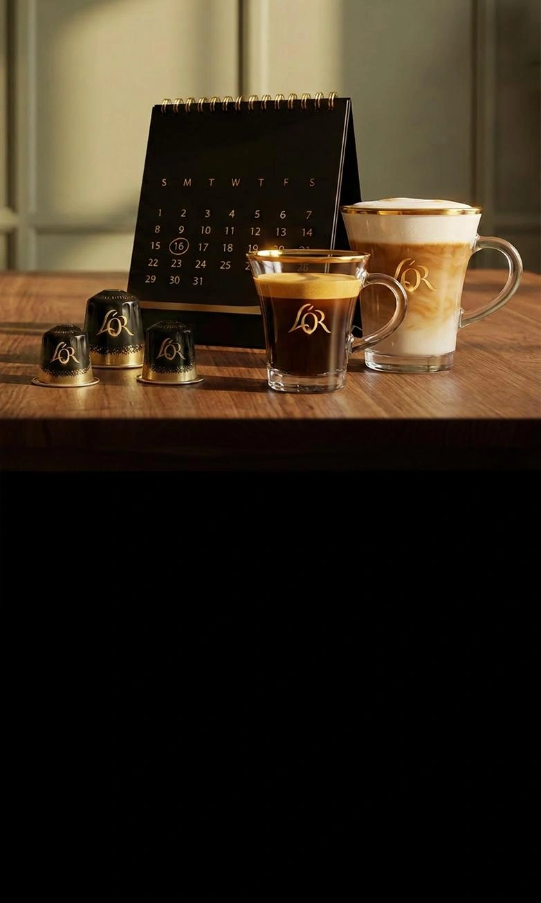 L'OR coffee capsules, an espresso and a latte macchiato next to a black desk calendar on a wooden table.
