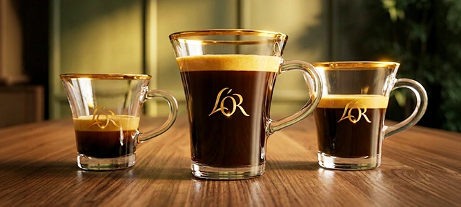 Three glass cups of L'OR coffee in different sizes, each marked with the L'OR logo, on a wooden table.