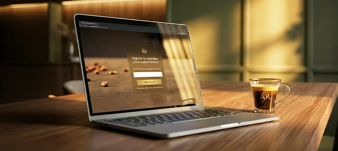 Laptop showing a subscription sign-in page next to a cup of L'OR espresso on a wooden desk.