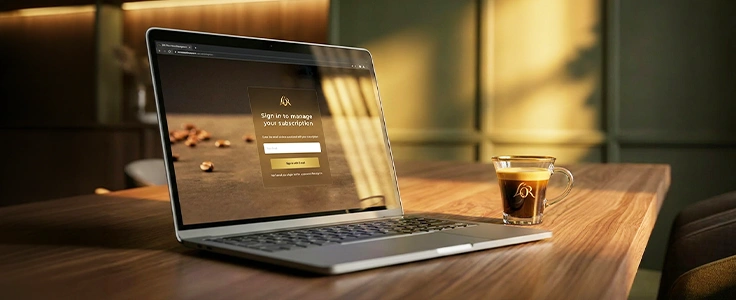 Laptop showing a subscription sign-in page next to a cup of L'OR espresso on a wooden desk.