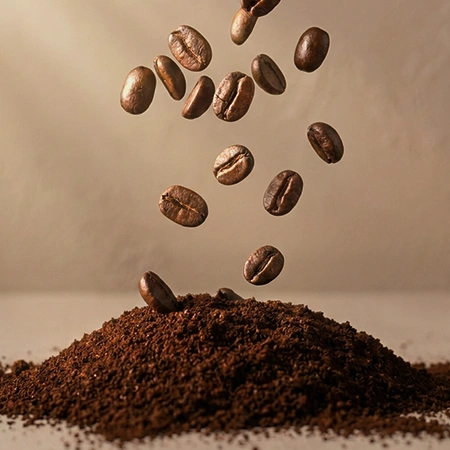 Coffee Beans falling on a pile of freshly grounded coffee