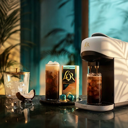 L’OR coffee machine preparing iced coffee with multiple drinks and capsules on a summer terrace at sunset