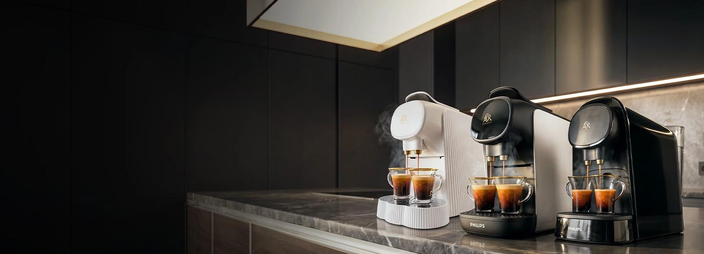 Two L’OR BARISTA coffee machines brewing espressos side by side on a dark gradient background.