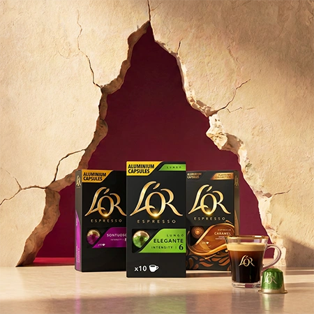Boîtes de capsules de café L'OR et tasses à café disposées devant un fond rouge festif.