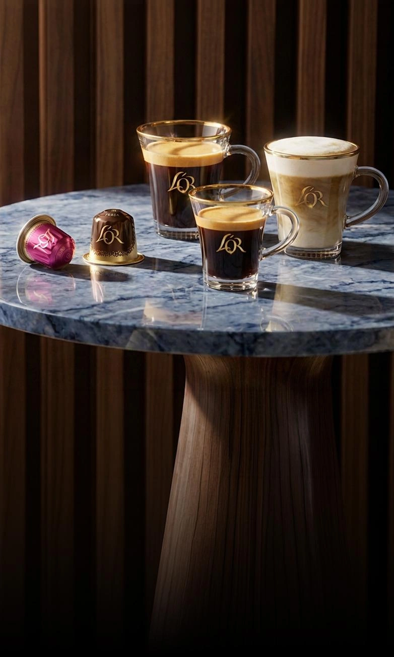 Three coffee drinks and L'OR capsules on a marble table against a dark wooden background.
