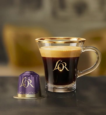 Purple L'OR coffee capsule beside a glass of black coffee.