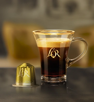 Yellow L'OR coffee capsule beside a glass of black coffee.