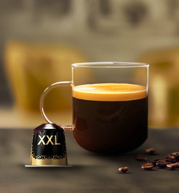 Glass of black coffee beside an L'OR Barista XXL capsule and coffee beans.
