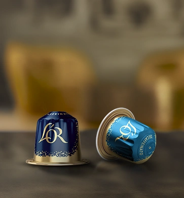 Two blue L'OR coffee capsules on a dark tabletop.