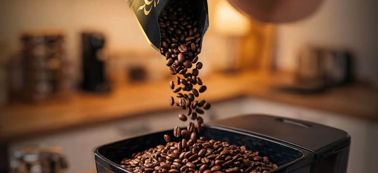 Roasted coffee beans falling into a coffee machine hopper.