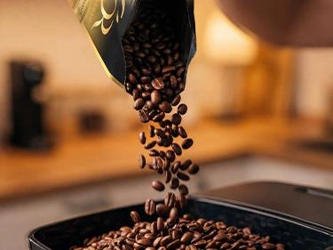 Roasted coffee beans pouring from an L’OR bag into a coffee machine hopper.