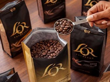 Close-up of a scoop of roasted coffee beans above an open L’OR bag.