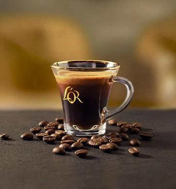 Glass cup of L’OR coffee surrounded by roasted coffee beans.