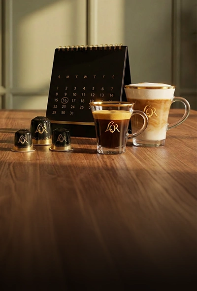 L'OR coffee capsules and coffee cups on the table top in front of a calendar