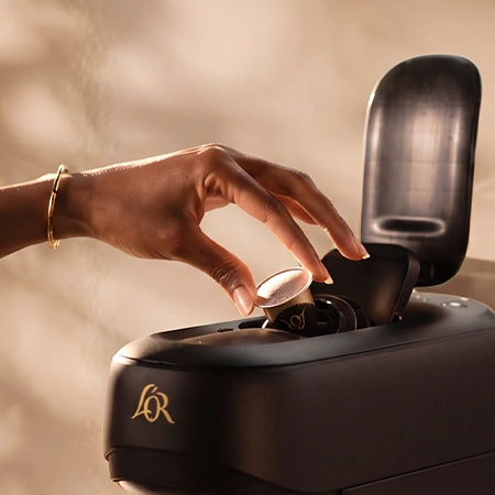 Hand placing an L'OR coffee capsule into a black coffee machine.