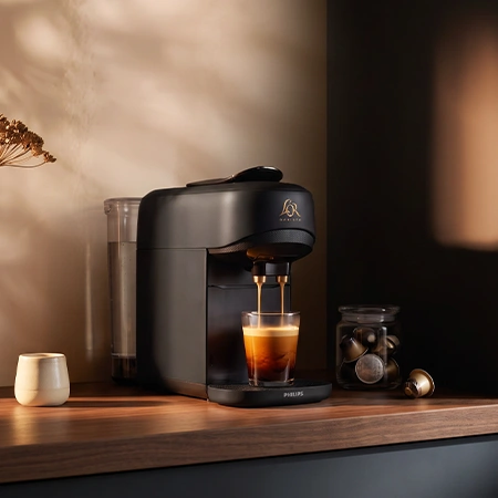 Black L'OR coffee machine dispensing espresso into a glass on a kitchen counter.