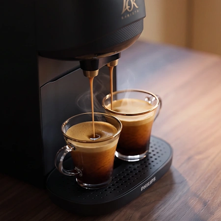 Two espresso glasses on the drip tray of a black L'OR coffee machine.