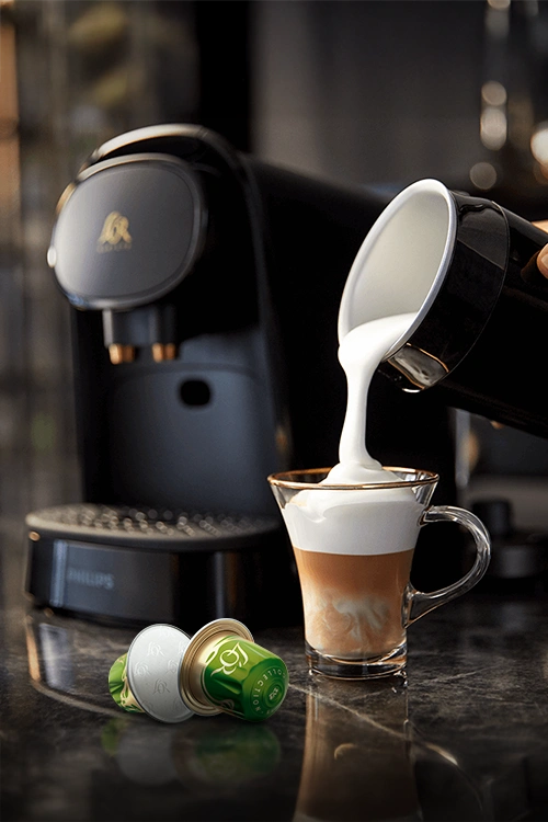 L'OR Milk Frother and few capsules from Flavours collection on a dark counter.